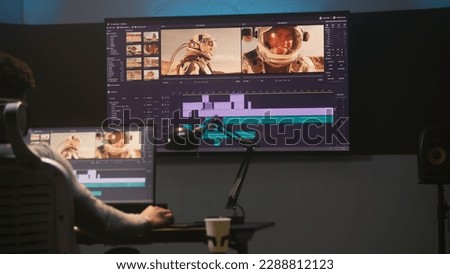 African American colorist makes color grading in video editing software. Multiple monitors with space travel film footage and RGB colour correction graphic bar. Movie post production in modern studio.