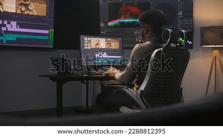 African American colorist makes color grading in video editing software. Multiple monitors with space travel film footage and RGB colour correction graphic bar. Movie post production in modern studio.