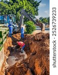 african american construction workers with an excavator fixing a blocked damaged broken drainage pipe in the trench outdoors