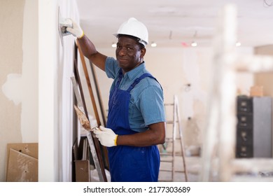 African American Contractor Doing Repairs In A New Building Plasters The Wall Indoors