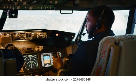 African american copilot flying airplane with captain in cockpit, throttling engine handle and fixing altitude and longitude. Navigation command on dashboard and control panel.