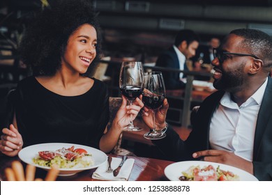 Afroamerikanischer Coupé im Restaurant. Romantisches Paar in Liebe Dating. Fröhlicher Mann und Frau mit Menü in einem Restaurant Making Order. Romantisches Konzept. Cheers Classes Red Wine.