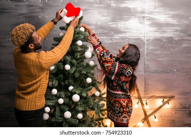 African American Couple Hanging Toys On A Christmas Tree