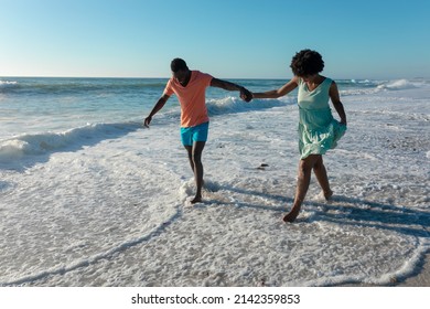 African american couple holding hands wading on shore at beach against sky during sunny day. unaltered, lifestyle, love, togetherness and holiday concept. - Powered by Shutterstock