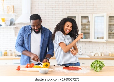 African American Couple Husband And Wife Having Fun Dancing In The Kitchen, Cooking Together At Home. Best Friends, Two People In Love Preparing Cooking Pizza, Guy Chopping Veggies, And Girl Moving