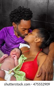An African American couple kiss while holding their brand new baby who was just born at home and still has the umbilical cord fresh and clamped.