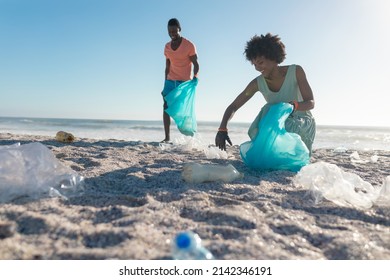 African American Couple Picking Up Garbage At Beach On Sunny Day. Unaltered, Togetherness, Responsibility And Environmental Issues Concept.