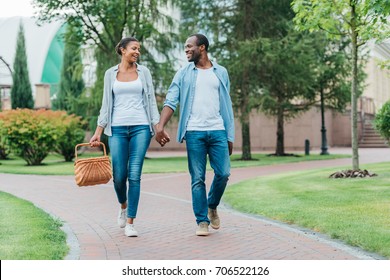 African American Couple With Picnic Basket Holding Hands While Walking In Park