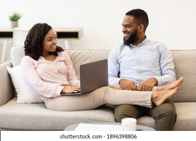 African American Couple Resting On Couch, Woman Using Laptop For Work Or Relax, Browsing Internet At Home. Female Lying Legs On Her Man Sitting On Sofa In Living Room. Love, Intimacy, Leisure - Shutterstock ID 1896398806
