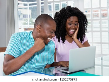 African American Couple Shopping Presents And Gifts Online With Laptop At Desk At Home