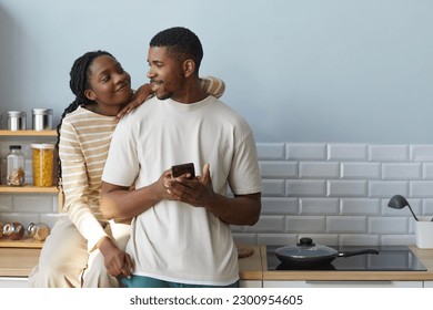 African American couple smiling and talking to each other while using smartphone, they spending time together at home - Powered by Shutterstock