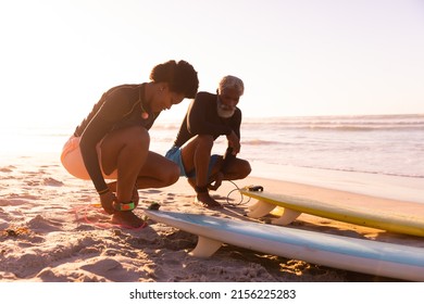 African american couple tying surfboards strings on ankles at beach against clear sky at sunset. copy space, nature, unaltered, love, togetherness, aquatic sport, holiday, active lifestyle concept. - Powered by Shutterstock