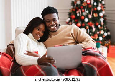 African American Couple Watching Christmas Movies On Laptop Computer Online Celebrating Xmas Eve At Home, Sitting On Sofa Covered With Blanket, Drinking Tea. Happy Family Enjoying New Year Evening - Powered by Shutterstock