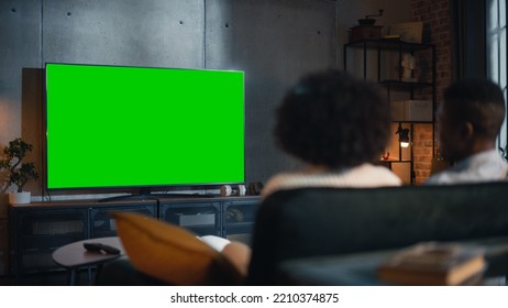 African American Couple Watching TV with Green Screen Mockup Display. They are Sitting on a Couch in Their Cozy Living Room and Eating Popcorn, Enjoying Movie on Streaming Service. Back View. - Powered by Shutterstock