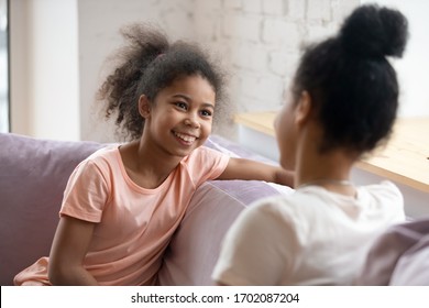 African American Cute Daughter Sitting On Sofa Talking With Mom. Diverse Happy Family Have Free Time Together. Mum And Teen Child Celebrate Mother Day In Private.