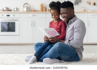 African American Dad And Child Celebrating Fathers Day At Home, Cheerful Handsome Black Man In Casual Sitting On Floor At Kitchen, Cuddling With His Little Daughter, Looking At Gift Card, Copy Space