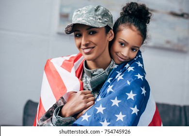 african american daughter and female soldier in military uniform wrapped with american flag at home