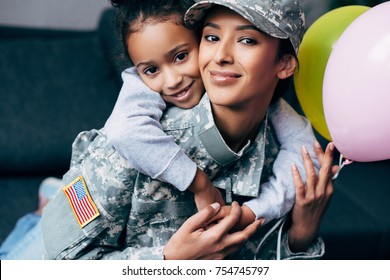 african american daughter hugging her mother in military uniform with balloons at home - Powered by Shutterstock