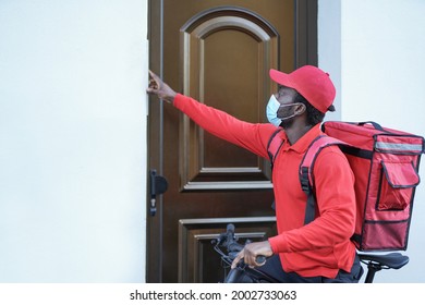 African American Delivery Man With Bicycle Ringing On Doorbell While Wearing Safety Face Mask For Coronavirus Outbreak