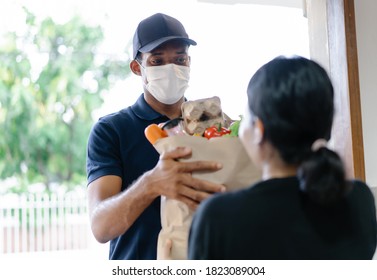 African American delivery man with medical mask delivering food to a woman at home.Online shopping and Express delivery. Under quarantine, disease outbreak, coronavirus covid-19 pandemic. - Powered by Shutterstock