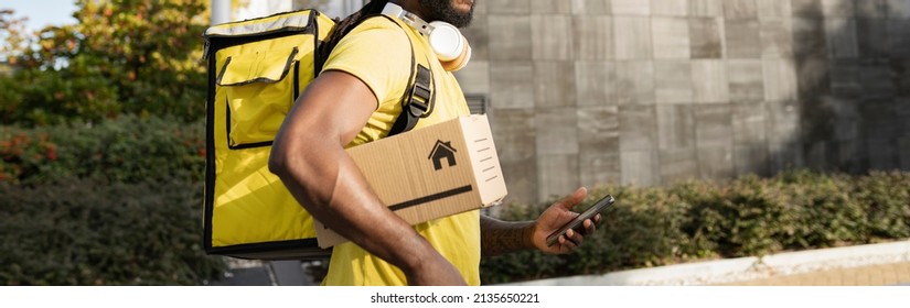 African American Delivery Man Walking With A Package And Mobile Phone Outside