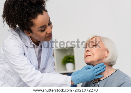 African american docktor in while coat checking neck of elderly patient