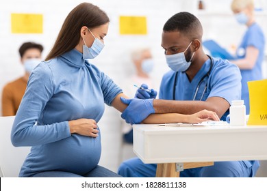 African American Doctor Giving Coronavirus Vaccine Injection Shot To Pregnant Woman, Wearing Protective Face Mask In Clinic Hospital. Corona Virus Vaccination, Patient Getting Vaccinated For Covid-19