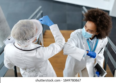 African American doctor and her colleagues wearing face masks and elbow bumping in hospital hallway.  - Powered by Shutterstock