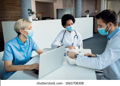 African American Doctor And Her Colleagues Wearing Face Masks And Talking During A Meeting At Medical Clinic. 