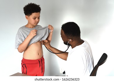 An African American Doctor With His Mixed Preteen Male.
A Cute Black Paediatrician Examining His Young Mixed Preteen Boy Patient With A Stethoscope.