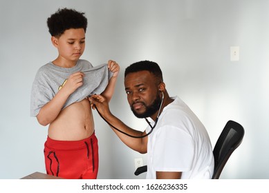 An African American Doctor With His Mixed Preteen Male.
A Cute Black Paediatrician Examining His Young Mixed Preteen Boy Patient With A Stethoscope.