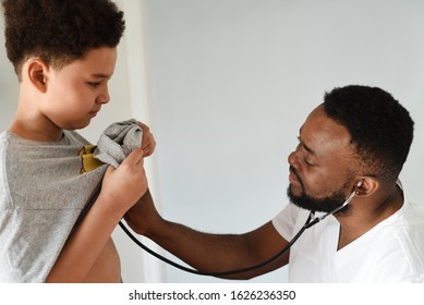 An African American Doctor With His Mixed Preteen Male.
A Cute Black Paediatrician Examining His Young Mixed Preteen Boy Patient With A Stethoscope.