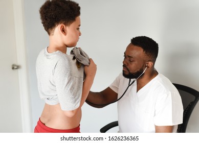 An African American Doctor With His Mixed Preteen Male.
A Cute Black Paediatrician Examining His Young Mixed Preteen Boy Patient With A Stethoscope.