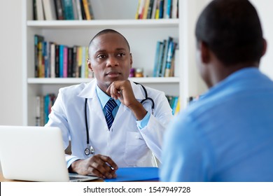 African American Doctor Listening To Problems Of Male Patient At Hospital