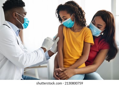 African american doctor making vaccination against coronavirus in shoulder for child, african american family in protective face masks visiting pediatrician at clinic. Kids immunization concept - Powered by Shutterstock