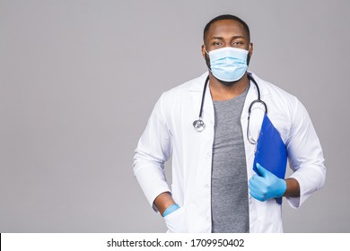 African american doctor man in face mask gloves isolated on grey background. Epidemic pandemic coronavirus 2019-ncov sars covid-19 flu virus. Holding clipboard. - Powered by Shutterstock