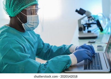 African American Doctor Man Using Computer Laptop Wearing Safety Mask At Work Inside Hospital - Focus On Keyboard