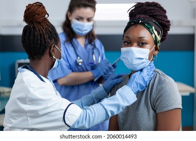 African american doctor mesauring cardiac pulse while cardiologist nurse writing healthcare treatment during clinical examination in hospital office. Women wearing face mask against coronavirus