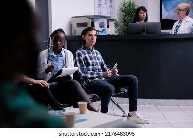 African American Doctor Talking With Patients At Hospital Reception Checking Appointments And Patients Priority. Asian Patient Waiting In Private Clinic While Medical Doctor Is Doing Clinic Triage.