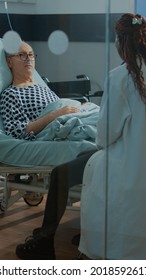 African American Doctor Talking To Sick Patient In Hospital Ward At Medical Facility. Old Man With Nasal Oxygen Tube And Oximeter Wanting Treatment For Disease, Heavy Health Problems