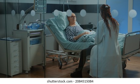 African American Doctor Talking To Sick Patient In Hospital Ward At Medical Facility. Old Man With Nasal Oxygen Tube And Oximeter Wanting Treatment For Disease, Heavy Health Problems