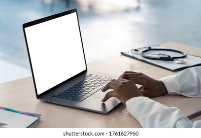 African american doctor wear white coat typing using laptop computer mock up white screen browsing internet sitting at work desk. Healthcare medical e health website technology concept. Close up view