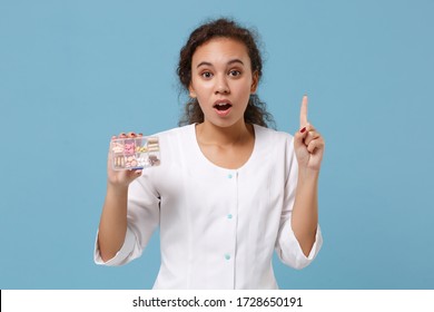 African American Doctor Woman Isolated On Blue Background. Female Doctor In Medical Gown Holding Finger Up With New Idea Hold Daily Pill Box. Healthcare Personnel Medicine Concept. Mock Up Copy Space