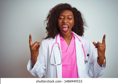 African American Doctor Woman Wearing  Pink Stethoscope Over Isolated White Background Shouting With Crazy Expression Doing Rock Symbol With Hands Up. Music Star. Heavy Concept.