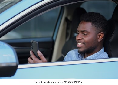 African American Driver With Phone Sitting At Car Steering Wheel. Bearded Man Spends Time In Traffic Jams Communicating With Friends.