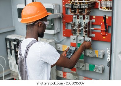African american electrician in safety helmet and glasses checking voltage in switchgear while working at solar station. Repairing of modern equipment. Production of green energy.