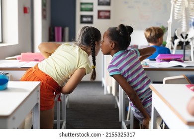 African American Elementary Girl Whispering To Caucasian Female Classmate At Desk In Classroom. Unaltered, Education, Childhood, Gossip, Secret, Sharing, Science, Stem And School Concept.