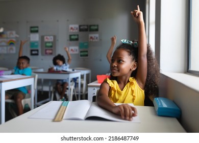 African american elementary school students with hands raised sitting at desk in classroom. unaltered, education, childhood, learning and school concept.