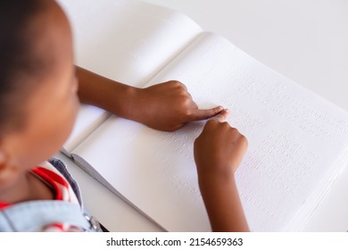 African american elementary schoolgirl touching braille book while studying at desk in class. unaltered, education, learning, studying, concentration, blind, and school concept. - Powered by Shutterstock