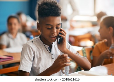 African American Elementary Student Making A Phone Call Via Cell Phone While Being On A Class At School. 